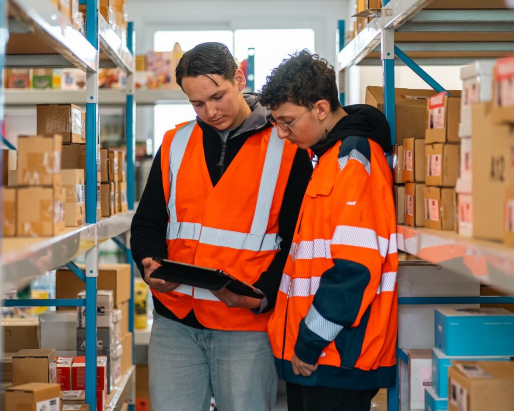 Deux élèves en gilet orange discutent dans les rayonnages de l'entrepôt pédagogique