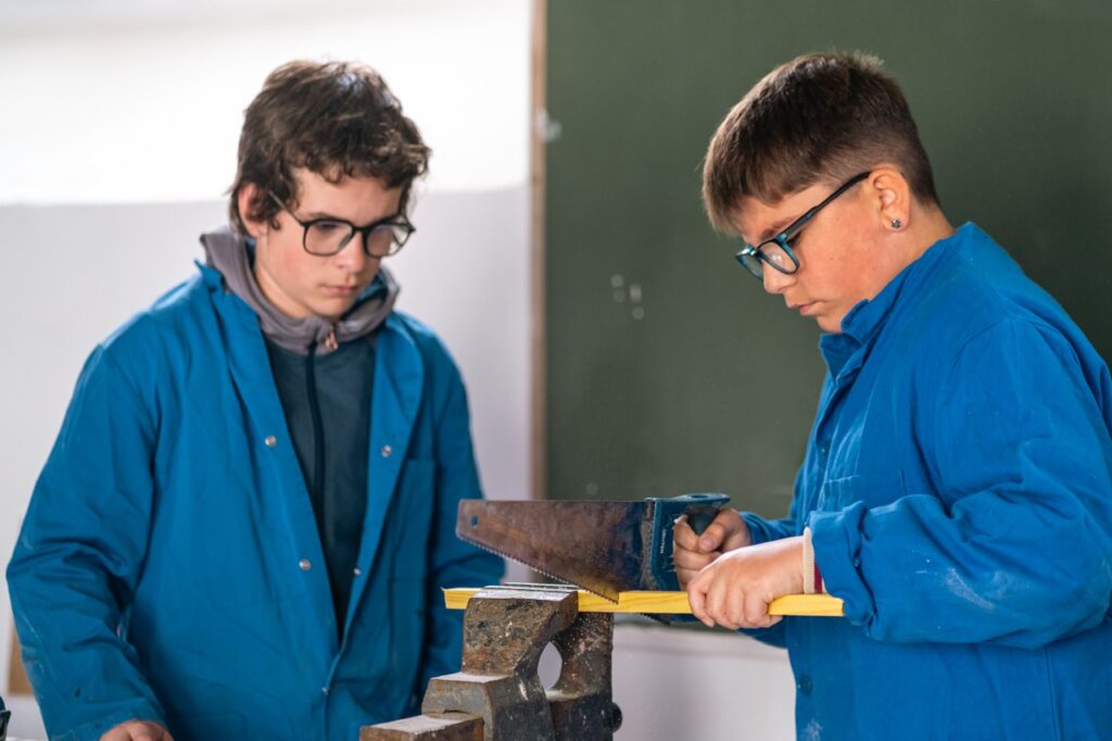 Deux élèves de SEGPA en blouse bleue travaillent le bois sur le plateau technique