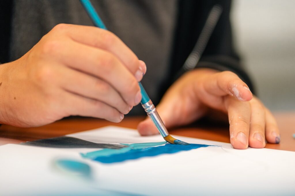 Un enfant peint une bande bleue au pinceau en atelier d'arts plastiques