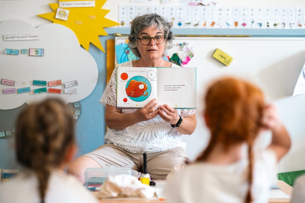 En maternelle, l'enseignante présente une image aux enfants assis au sol
